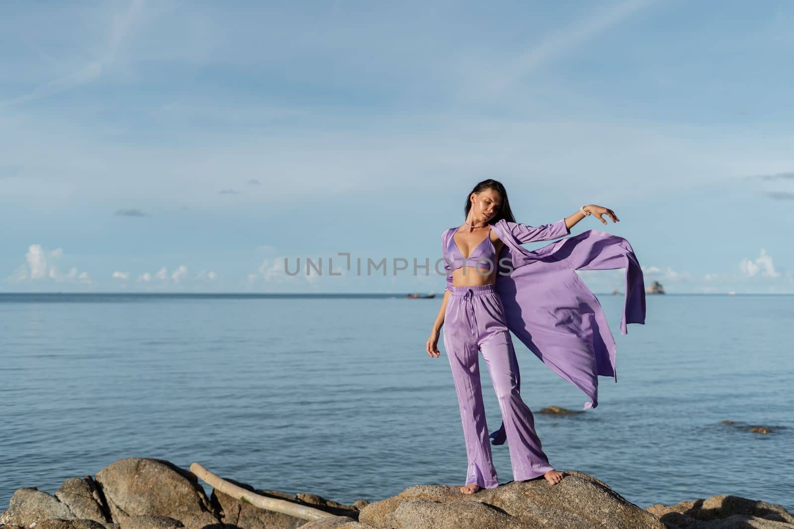 Young beautiful woman in a romantic mood, lilac silk clothes, on the beach against the backdrop of the sea and stones at sunset by kroshka_nastya