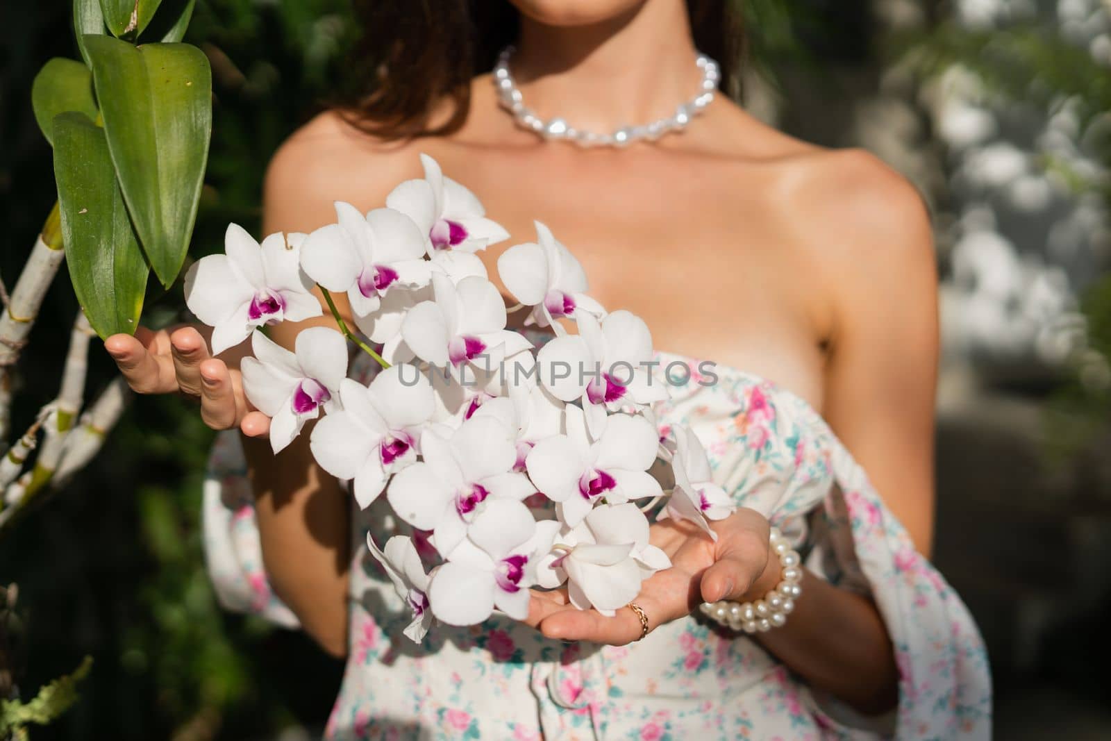 Young beautiful woman in a romantic dress with a floral print, and a pearl necklace bracelet, a close shot of hands and flowers