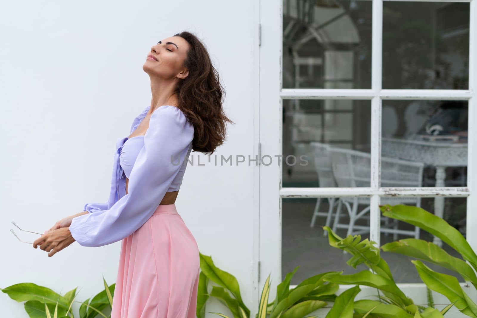Pretty young stylish woman in trendy purple crop top long sleeve , pink skirt, isolated, white wall, tropical leaves natural day light.. by kroshka_nastya