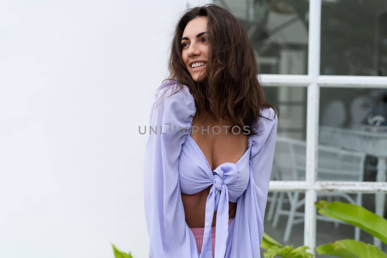 Pretty young stylish woman in trendy purple crop top long sleeve , pink skirt, isolated, white wall, tropical leaves natural day light..