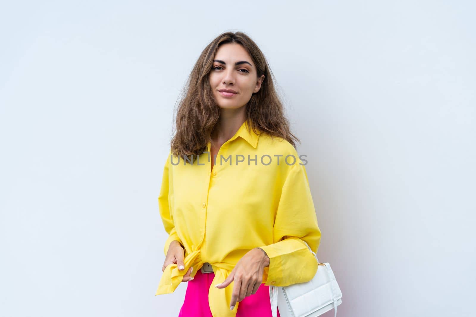 Stylish fit fashion women in yellow shirt and bright pink pants holding bag trendy posing on white wall background outdoor natural day light by kroshka_nastya