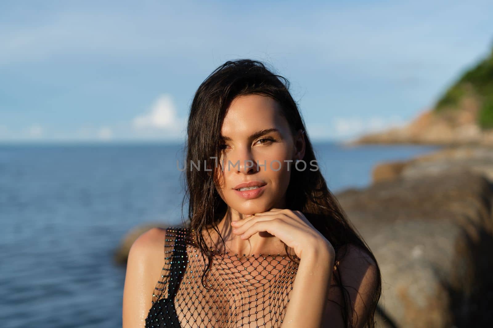 Young beautiful tanned woman on the background of the sea at sunset in a black swimsuit and a mesh dress