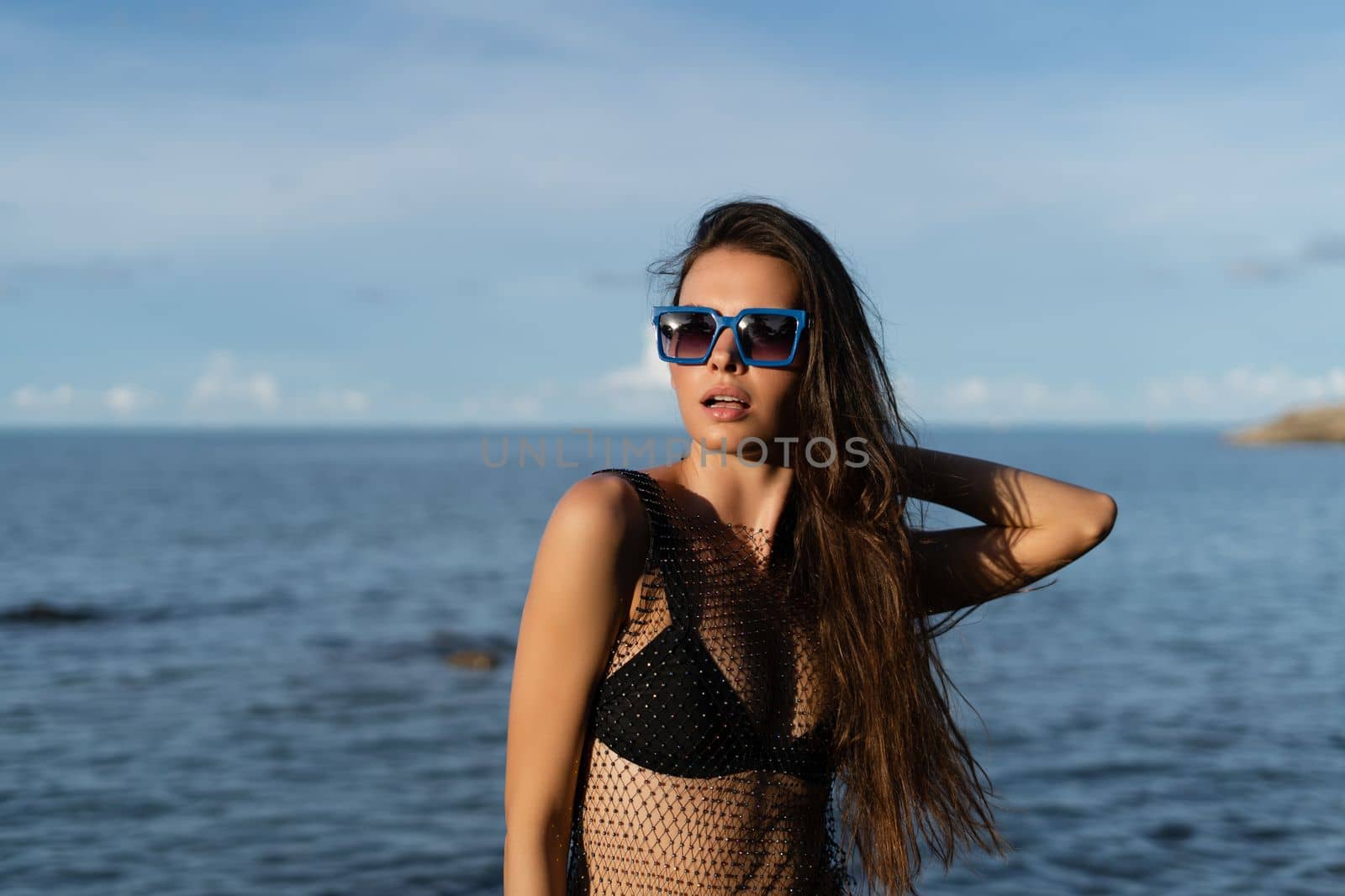 Young beautiful tanned woman on the background of the sea at sunset in a black swimsuit and a mesh dress by kroshka_nastya