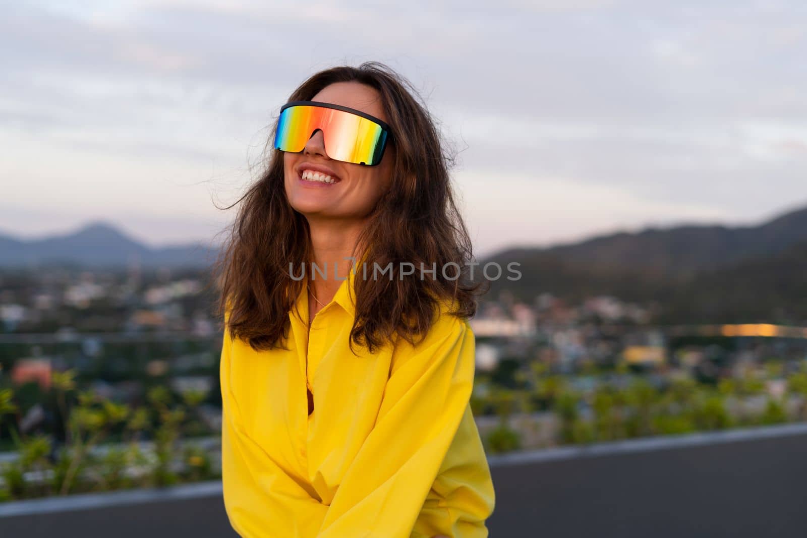 Stylish fit fashion women in bright yellow shirt trendy shield visor rainbow sunglasses posing at rooftop terrace tropical view outdoor sunset warm light by kroshka_nastya