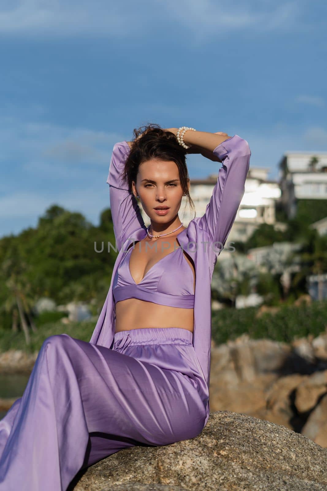 Young beautiful woman in a romantic mood, lilac silk clothes, on the beach against the backdrop of the sea and stones at sunset