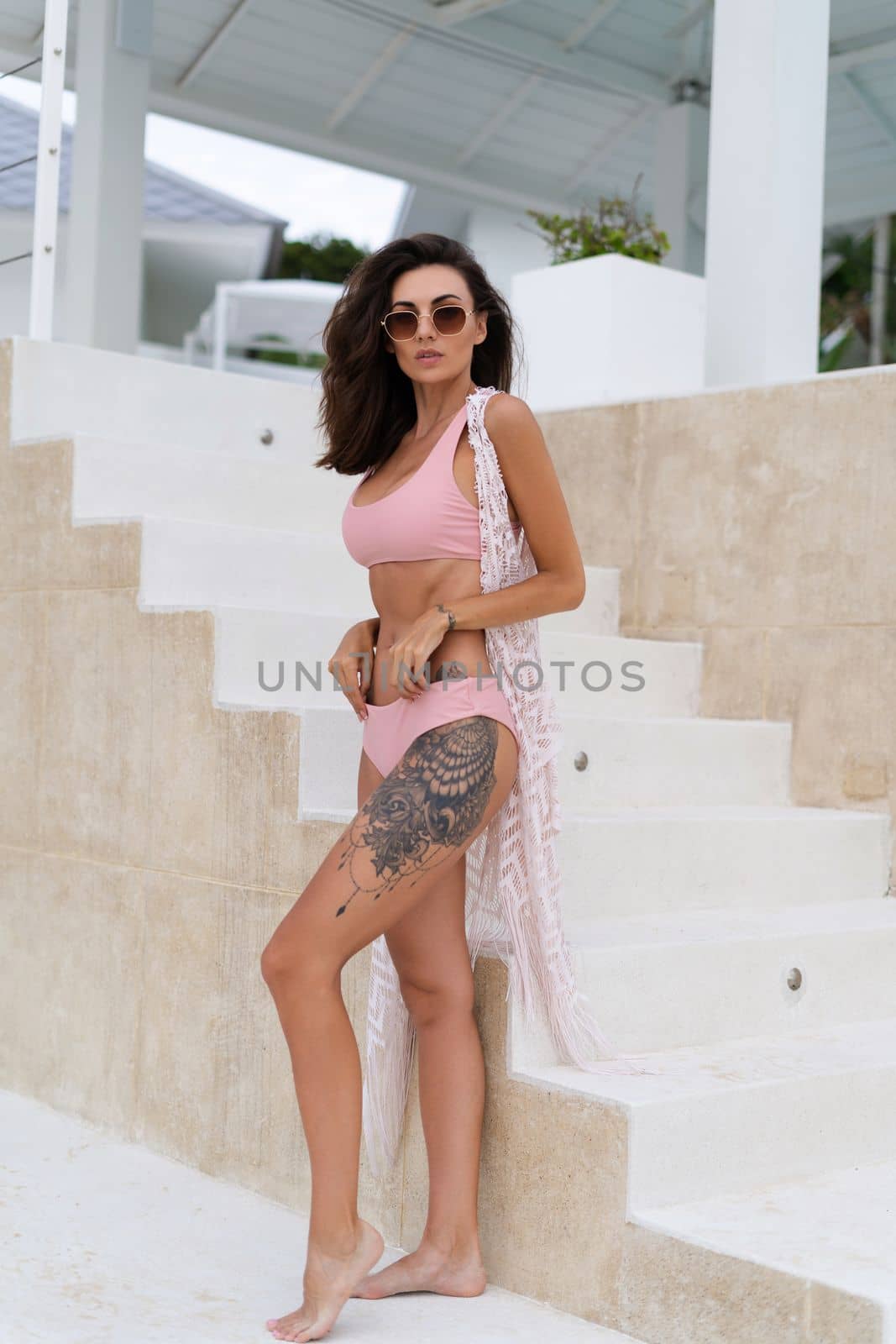 Stylish young woman with voluminous hair in a bikini and lace pareo posing in a hotel, big tattoo on her thigh, skinny, tanned, athletic, sunglasses by kroshka_nastya