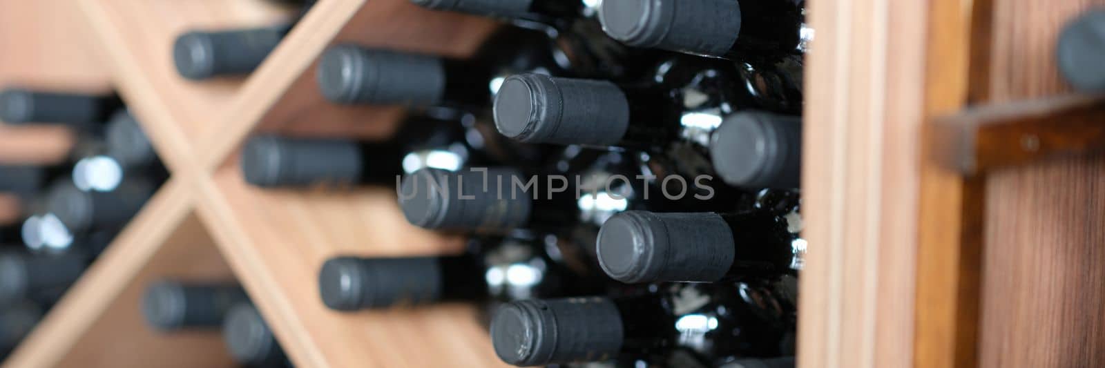 Red wine bottles stacked on wooden racks closeup. Most expensive varieties and brands of wines concept