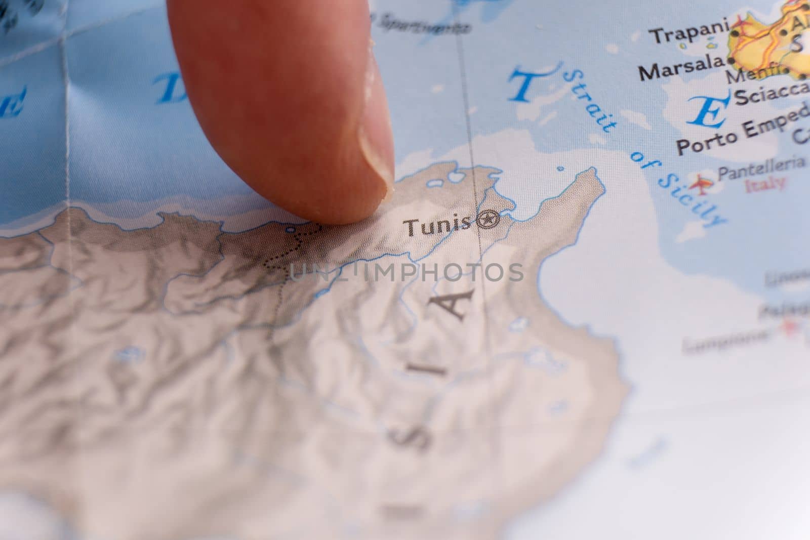 Finger pointing to Tunis, Tunisia on detailed colorful map with shallow depth of field, background blur. Concept geopolitical tensions. High quality photo