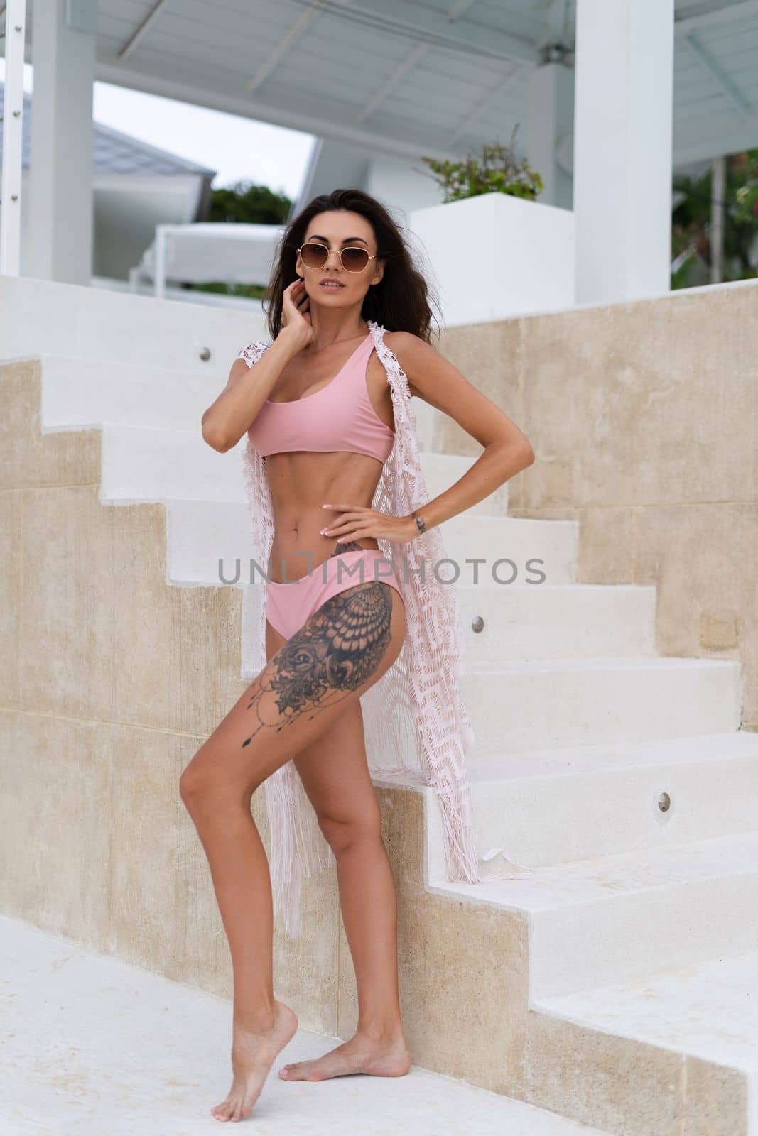 Stylish young woman with voluminous hair in a bikini and lace pareo posing in a hotel, big tattoo on her thigh, skinny, tanned, athletic, sunglasses by kroshka_nastya