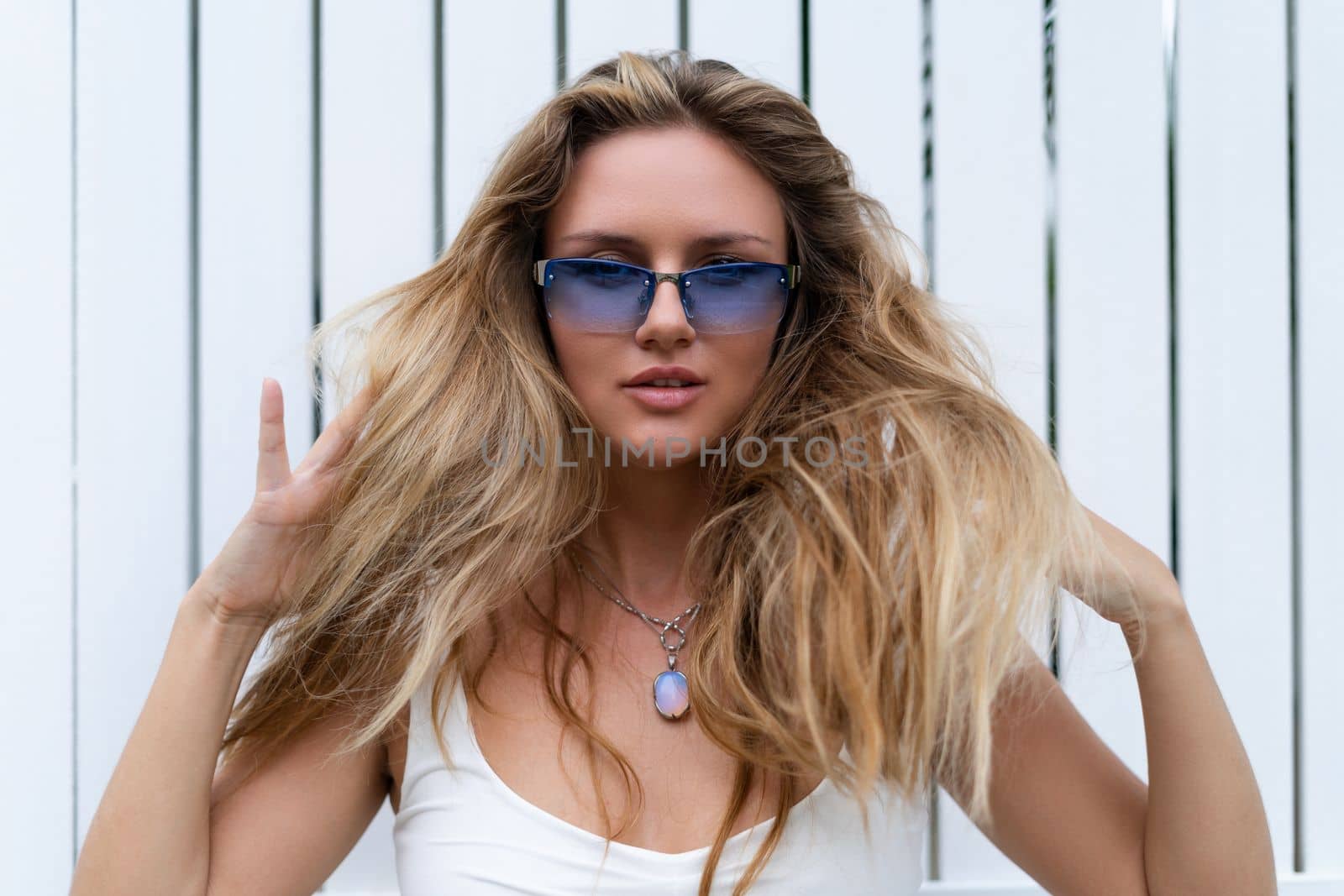 Beautiful young blonde woman in a top with long hair and smooth clean soft skin, natural beauty, daylight, wearing blue glasses, posing against the backdrop of a wooden fence by kroshka_nastya