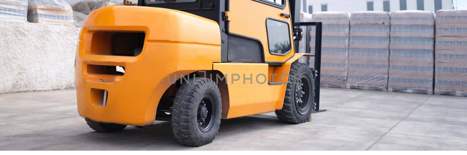 Reliable yellow forklift in warehouse. Worker ready to load pallets with skid steer loader concept