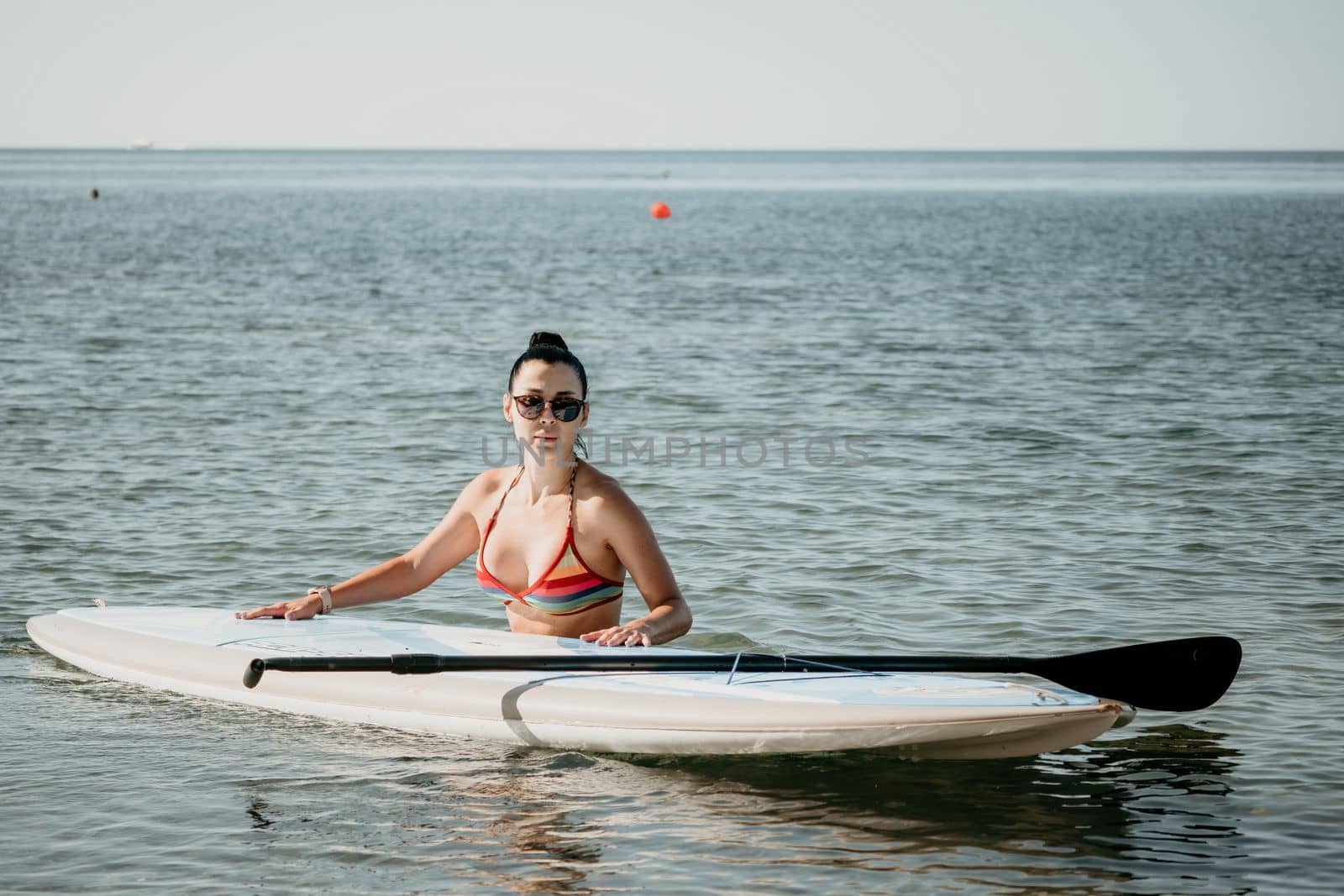 Sea woman sup. Silhouette of happy middle aged woman in rainbow bikini, surfing on SUP board, confident paddling through water surface. Idyllic sunset. Active lifestyle at sea or river