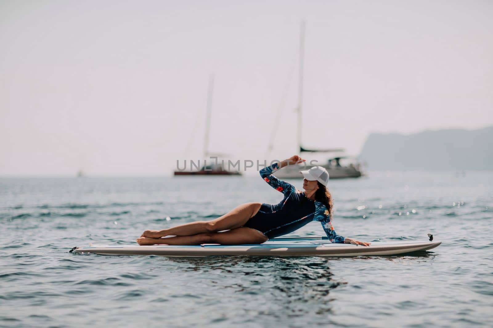 Woman sup yoga. Middle age sporty woman practising yoga pilates on paddle sup surfboard. Female stretching doing workout on sea water. Modern individual hipster outdoor summer sport activity