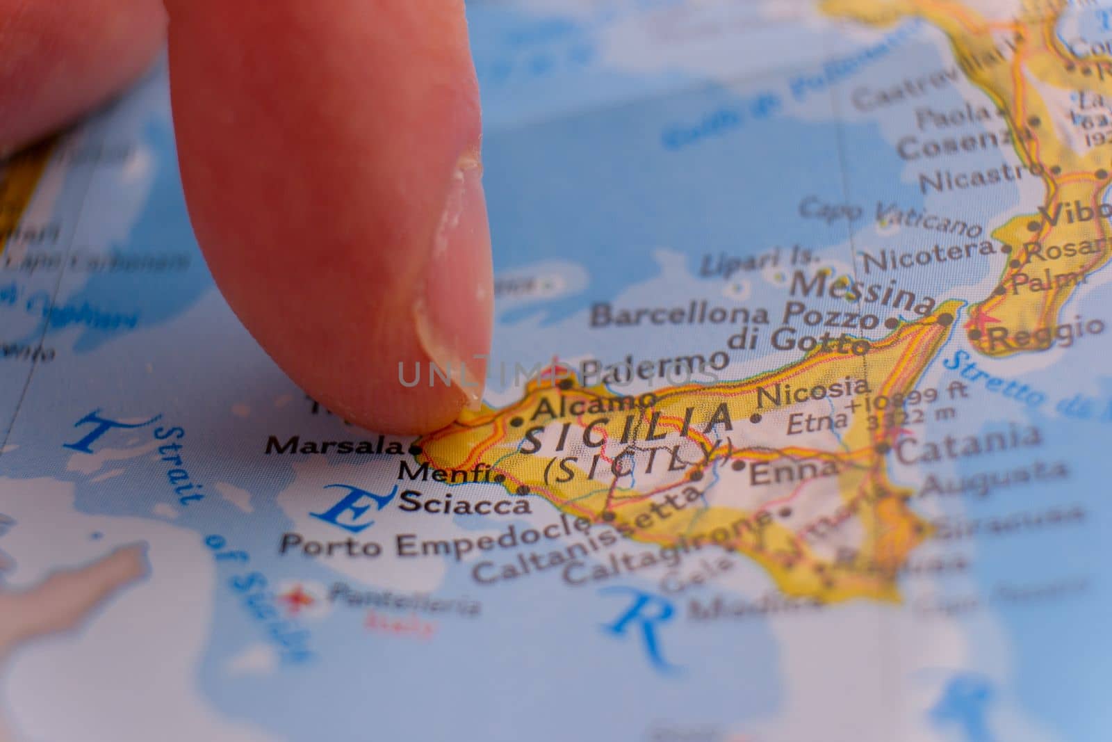 Close up of finger pointing to Sicily, Italy with shallow depth of field, background blur. Concept geopolitics. High quality photo