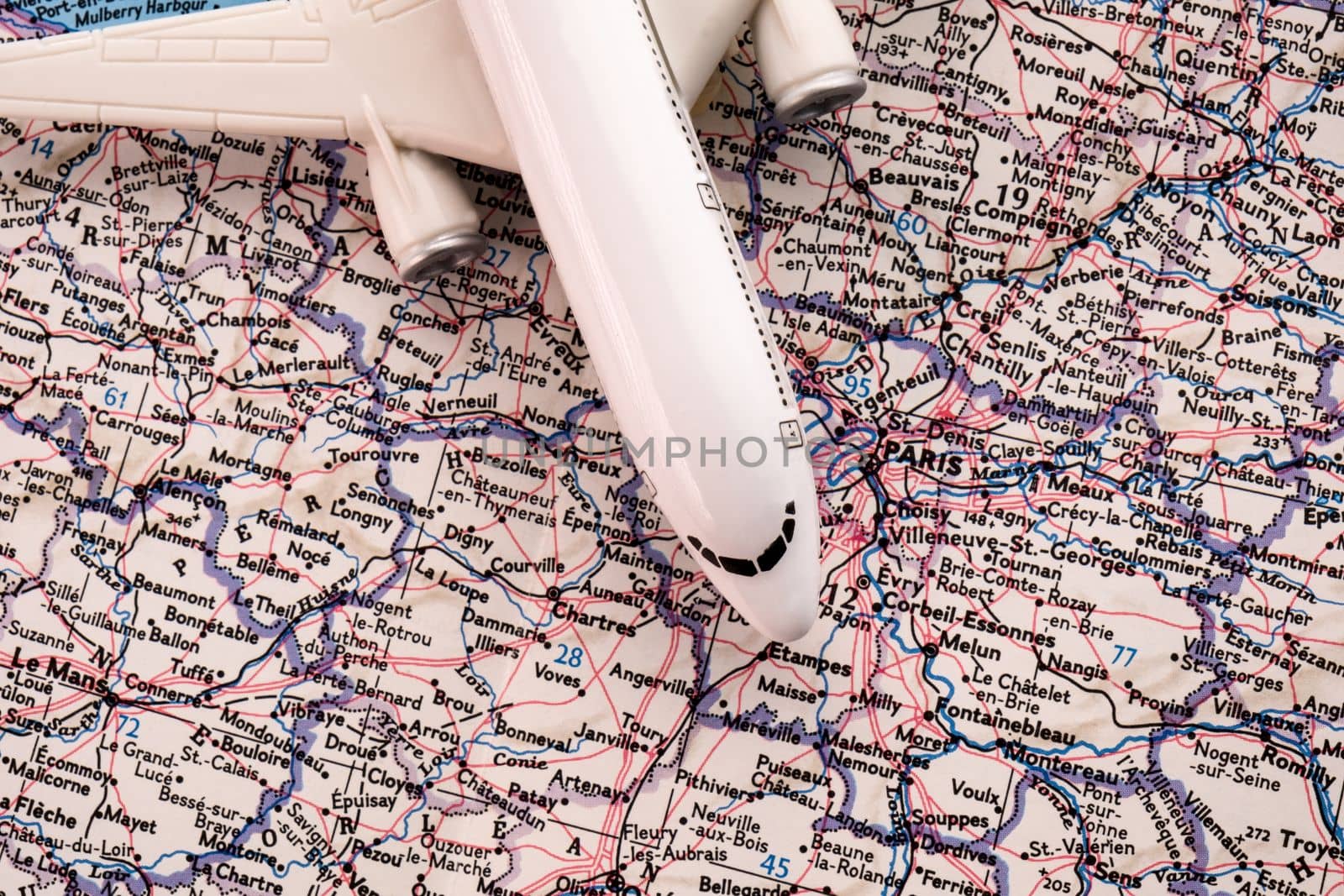Bird's eye close up of a miniature passenger plane on a colorful detailed map showing Paris, France. High quality photo