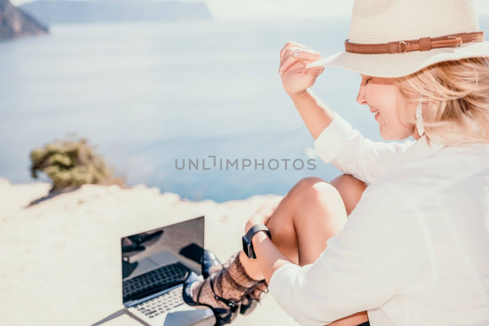 Woman sea laptop. Business woman in yellow hat freelancer with laptop working over blue sea beach. Girl relieves stress from work. Freelance, digital nomad, travel and holidays concept by panophotograph