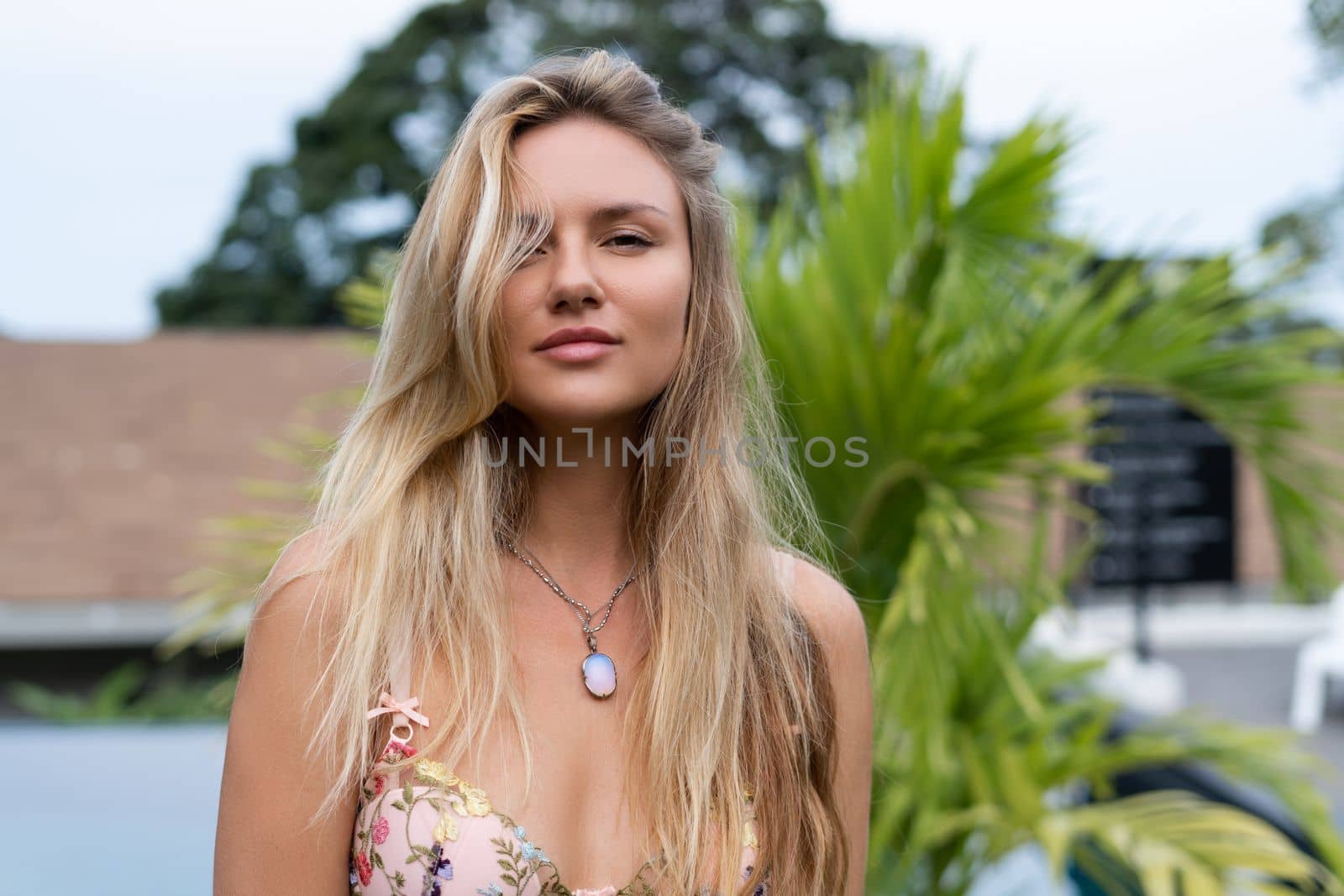 Beautiful young blonde in a top with long hair and smooth clean soft skin, natural beauty, daylight, pendant on neck accessory, posing with palm leaf