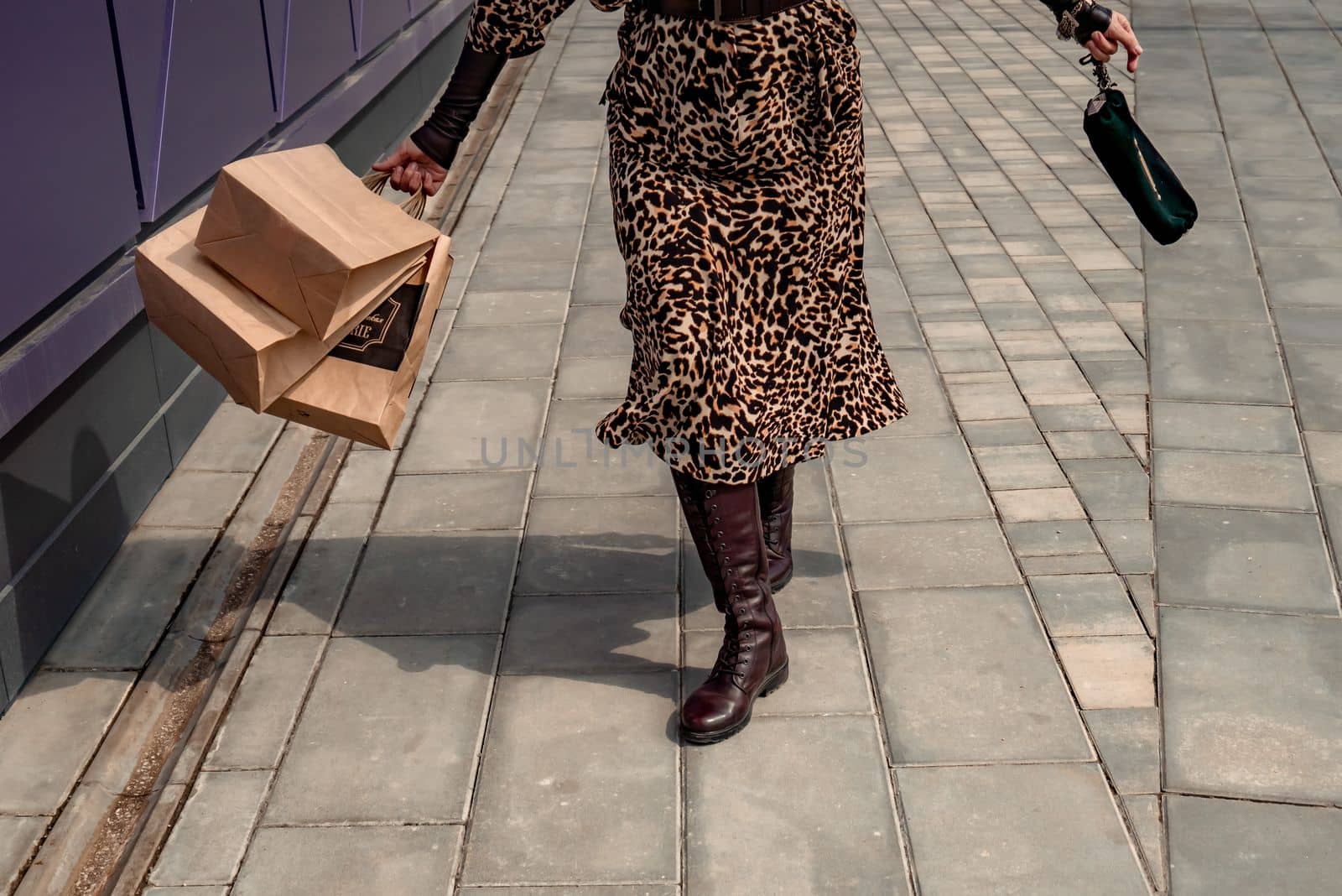 A happy shopaholic girl keeps her bags near the shopping center. A woman near the store is happy with her purchases, holding bags. Dressed in a leopard print dress. Consumer concept