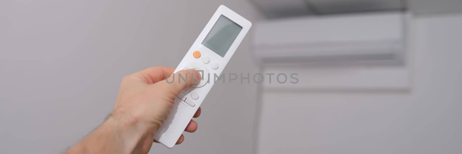 Hand with the remote control is directed to air conditioner by kuprevich