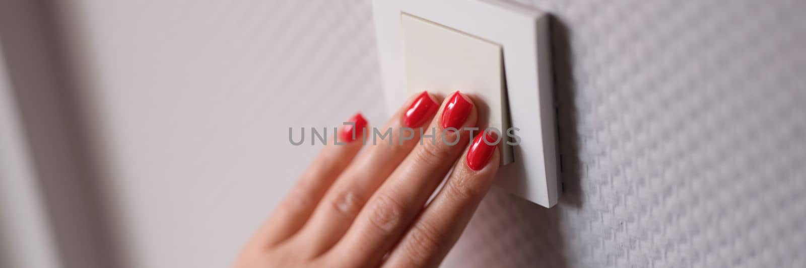 Female hand presses white switch on gray wall closeup. Saving electricity at home concept