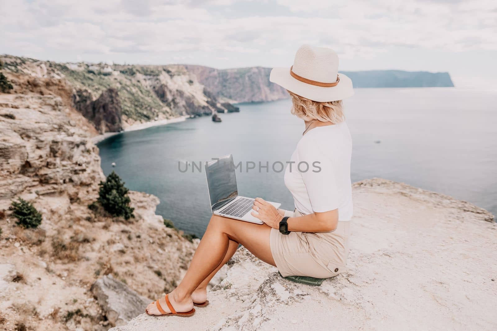 Digital nomad, Business woman working on laptop by the sea. Pretty lady typing on computer by the sea at sunset, makes a business transaction online from a distance. Freelance remote work on vacation