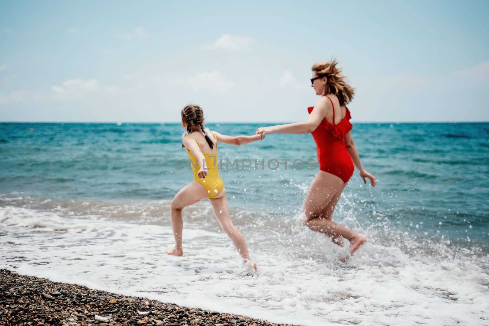 Happy loving family mother and daughter having fun together on the beach. Mum playing with her kid in holiday vacation next to the ocean - Family lifestyle and love concept.