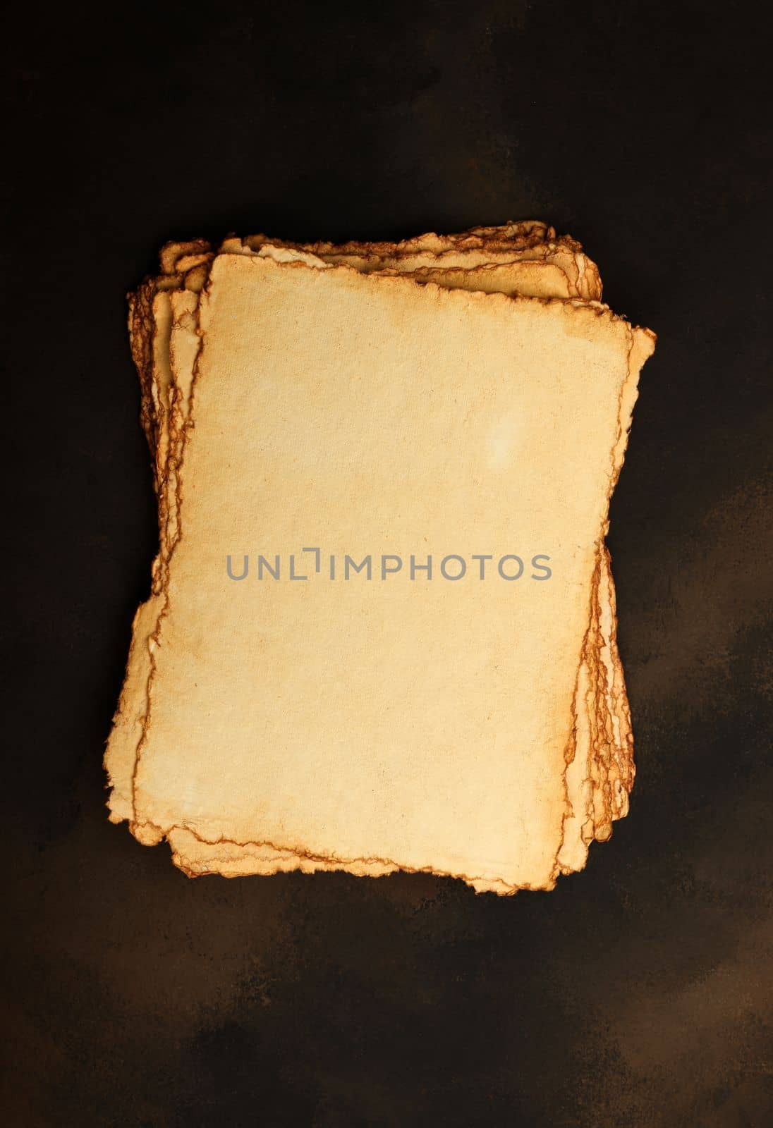 Close up stack of several blank old antique vintage brown paper parchment sheets with aged and weathered edges over dark table background