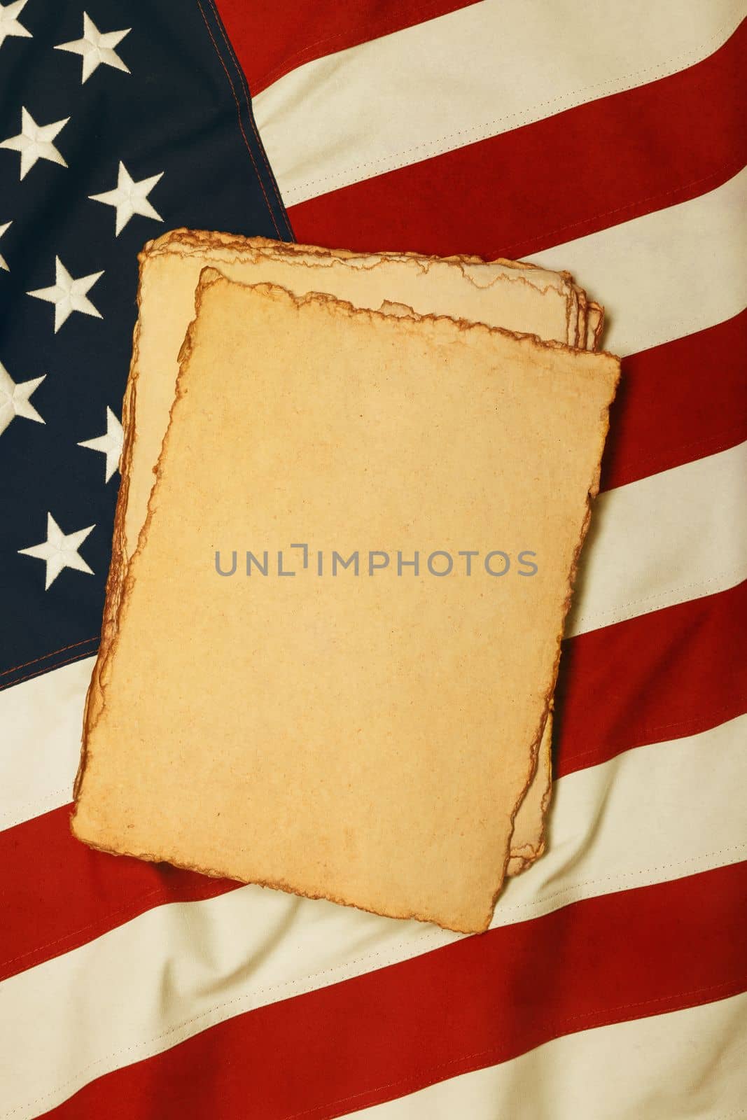 Close up heap of blank vintage yellow paper sheets on old weathered cotton embroidered US national flag, symbol of American history, elevated high angle view, directly above