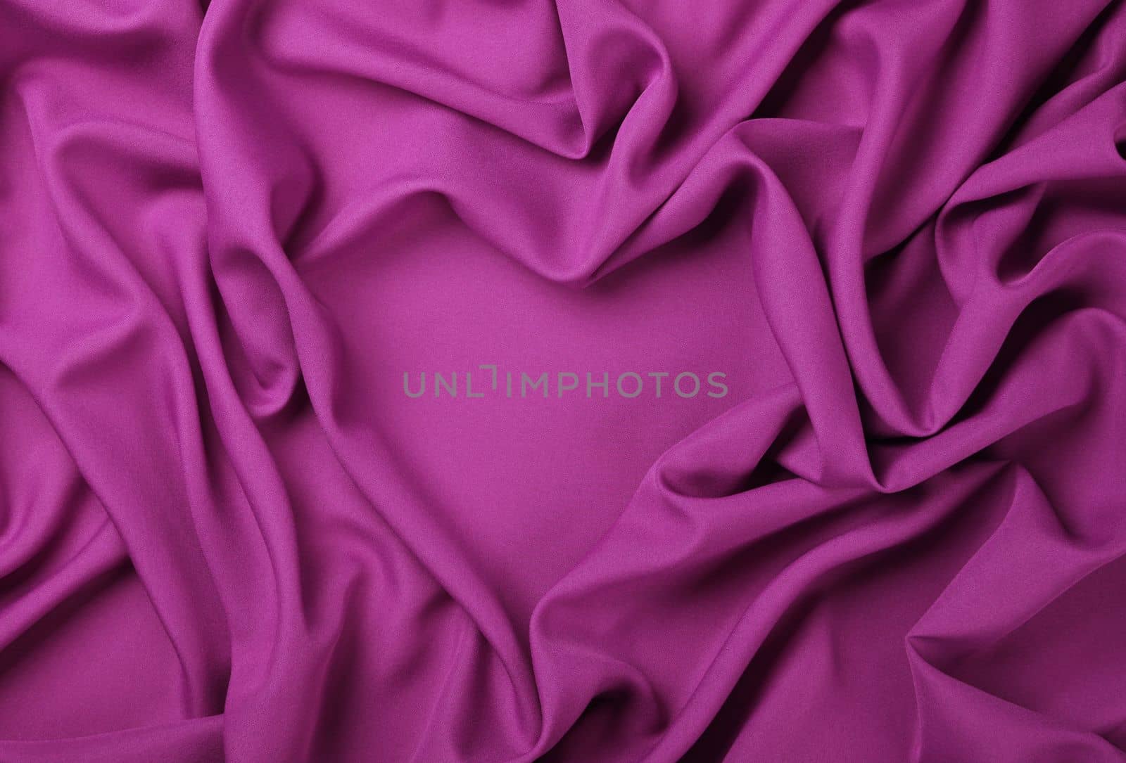 Close up abstract textile background of heart shaped purple pink folded pleats of fabric, elevated top view, directly above