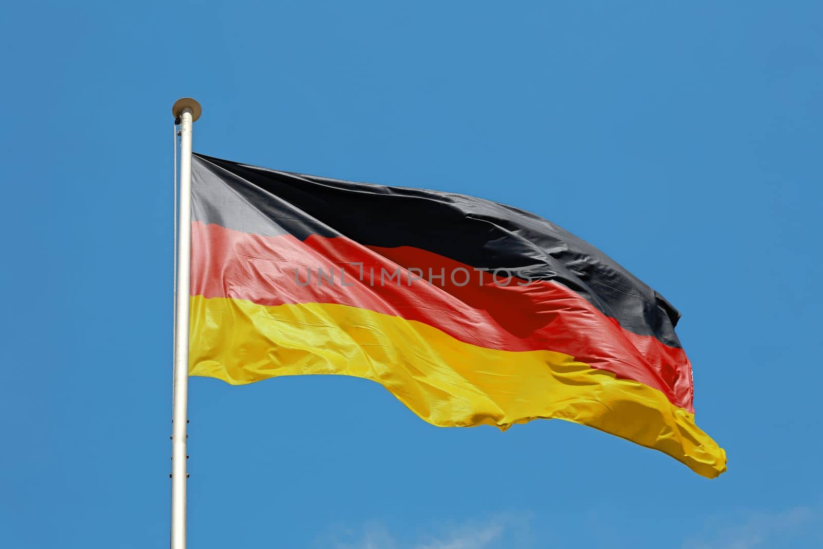 National flag of Germany flying and waving in the wind on flagstaff over clear blue sky, symbol of German patriotism, low angle, side view