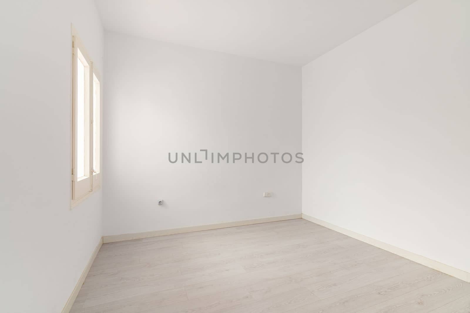 View of an empty white bright room with window without furniture after painting and renovation with wooden floor and baseboards. Concept of beautiful laconic interior for various inspiring ideas.