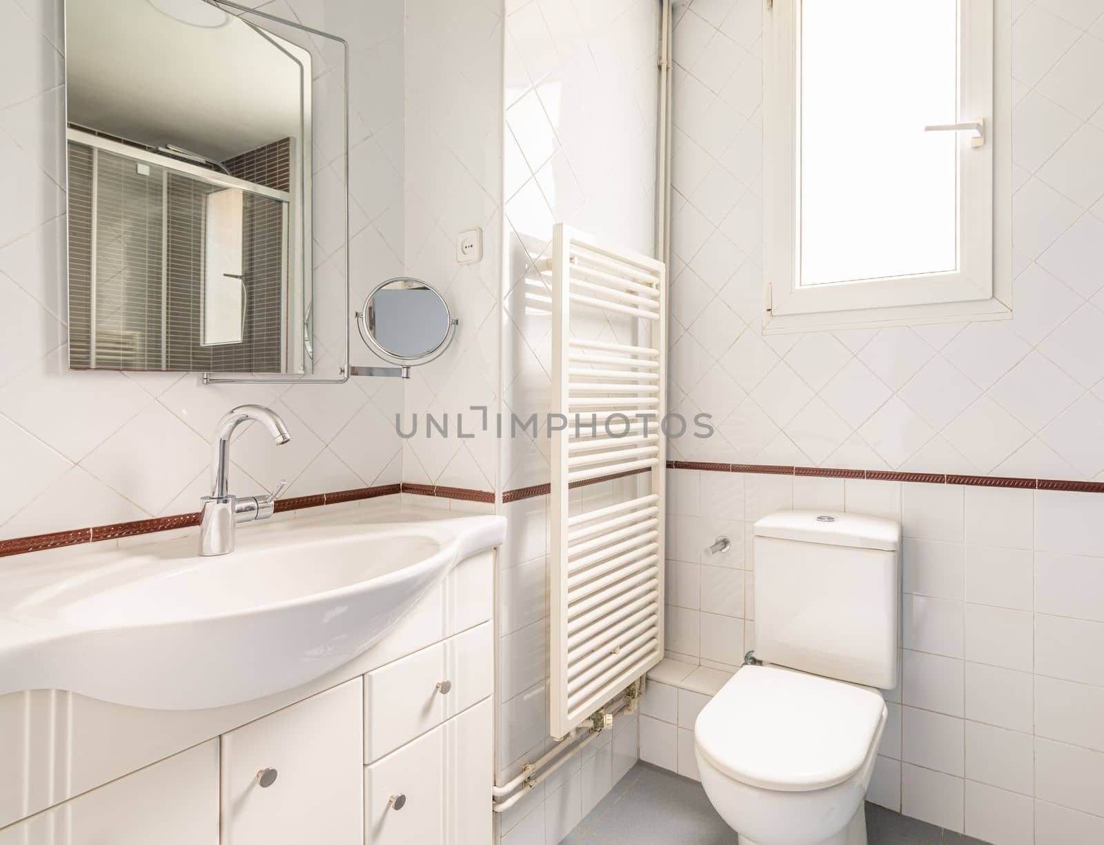 Cozy bright white bathroom with diamond shaped tiles with a window for natural light toilet sink and heated towel rail and mirror. Concept of modern cozy bathroom.