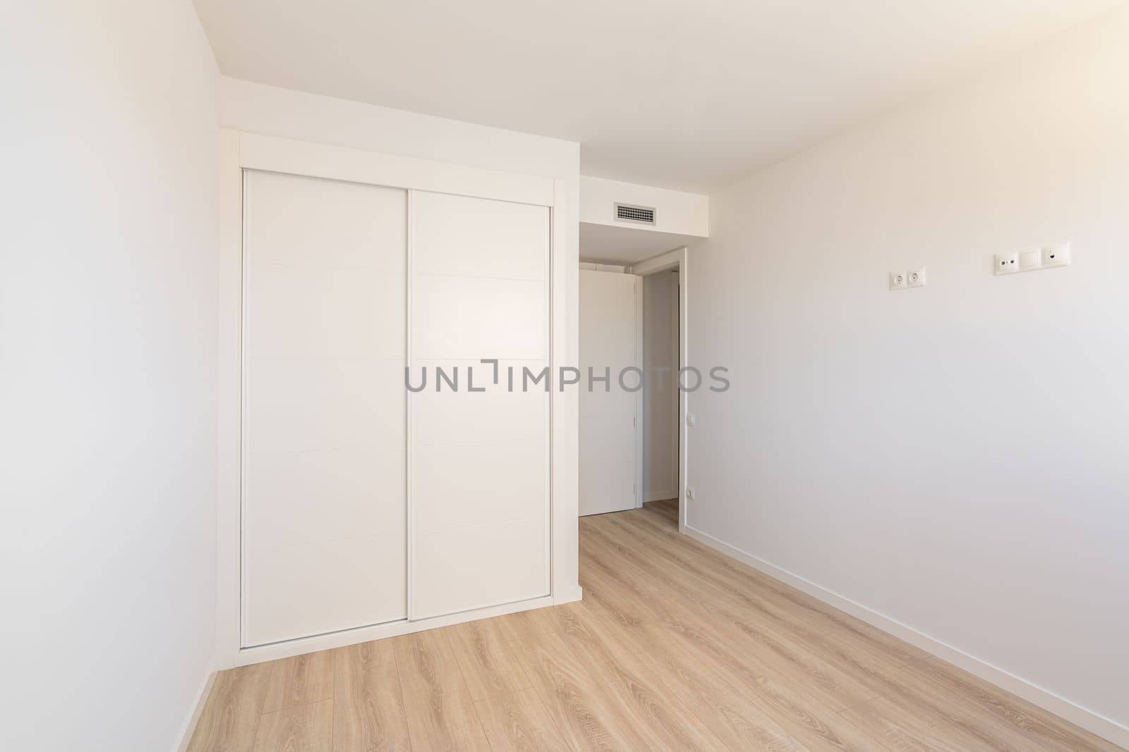 White empty sunny room with built-in wardrobe ventilation and two doors to the bathroom and exit. Concept of a new building or real estate for rent.