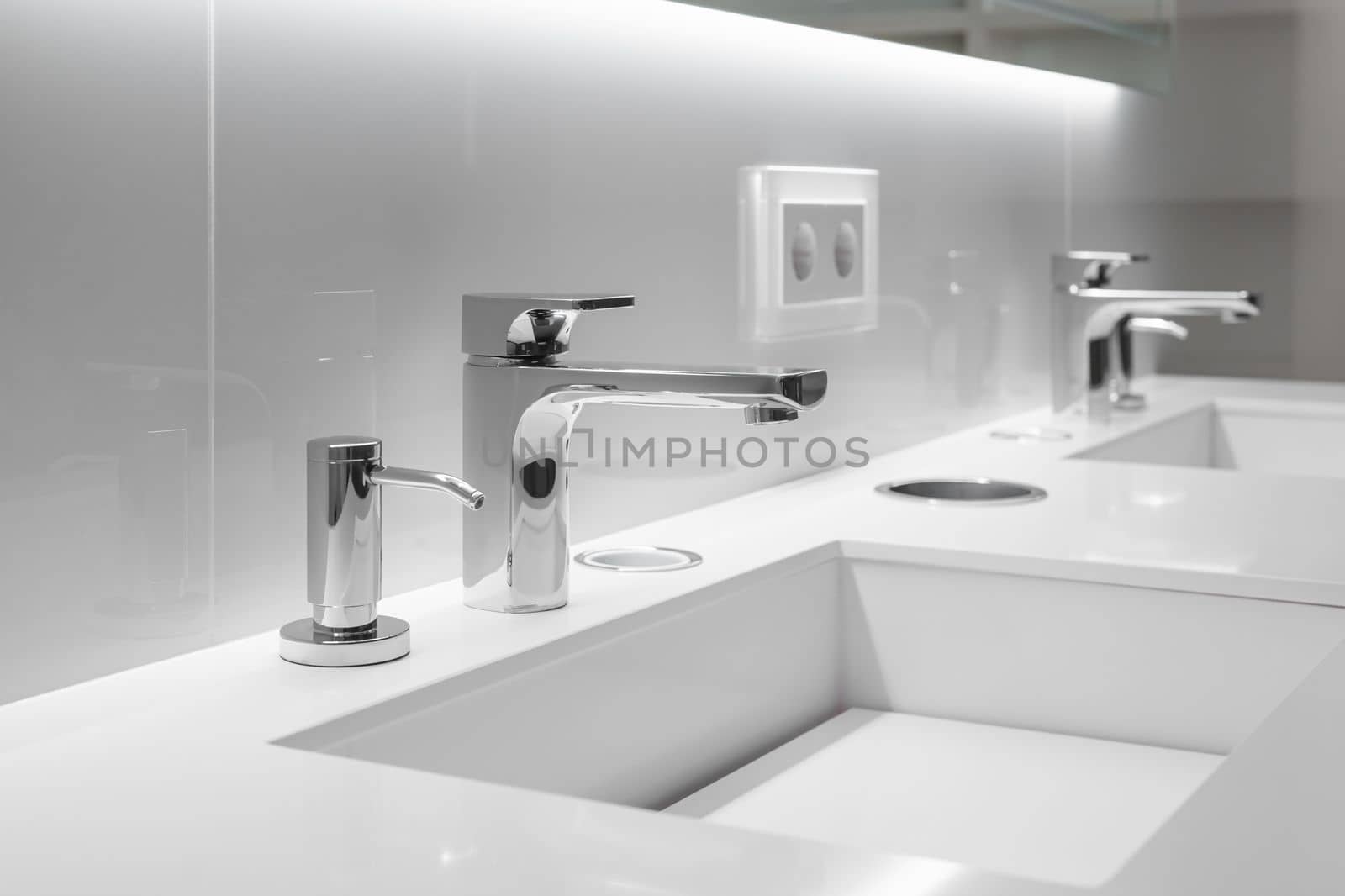 Close-up of two stylish sinks with faucets in white bathroom with a bevelled mirror and backlight. Concept of a modern stylish bathroom for a hotel or spacious home.