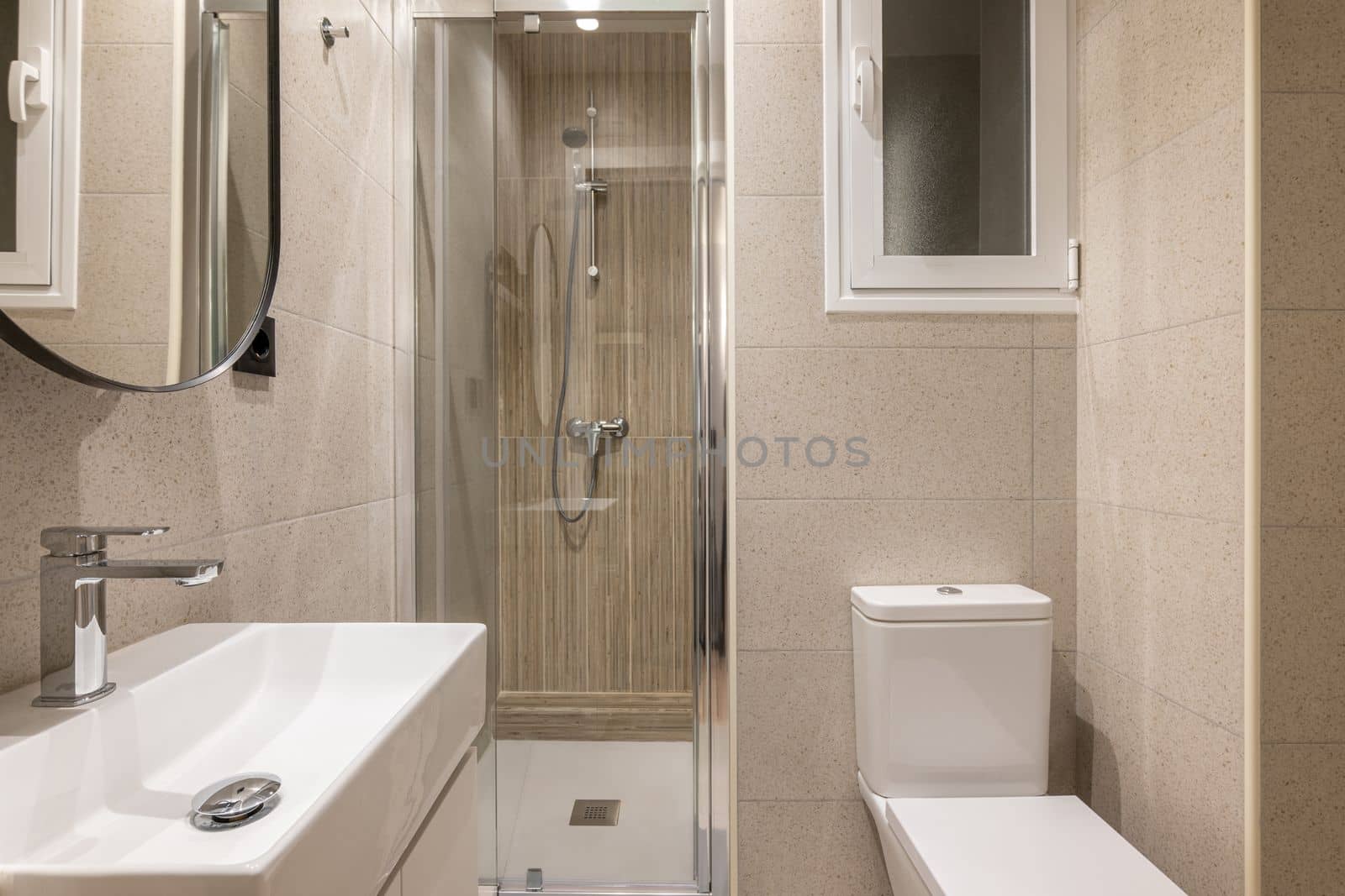 Beautiful fresh and comfortable bathroom for water procedures, morning and evening exercise. Room in beige tones with large sink, beautiful mirror, glass shower and white toilet