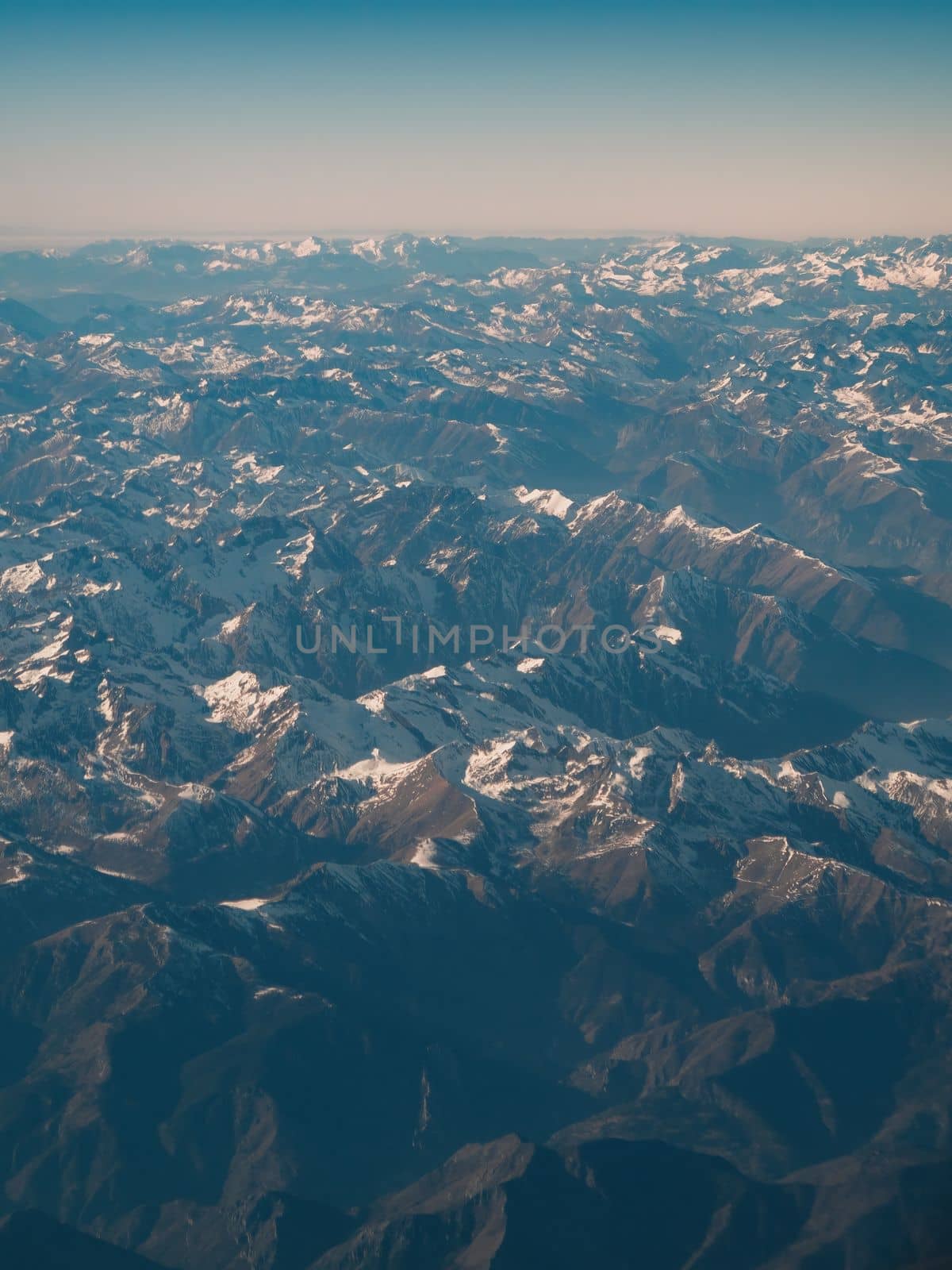 Amazingly beautiful panoramic aerial view of snow-capped mountain ranges of Alps. Flight over Alpine mountain peaks covered with snow in places. Mountain range to horizon with azure sky. by apavlin