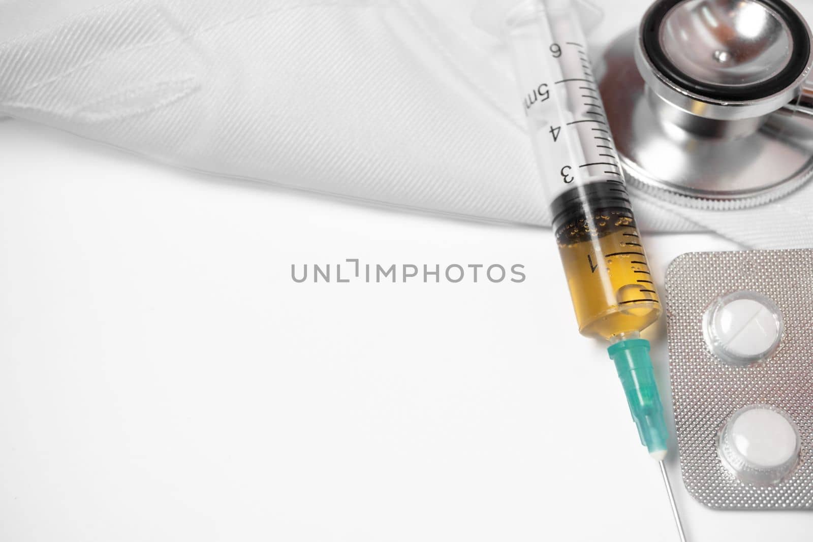 syringe, stethoscope and pills on a doctor's gown white background and copy space