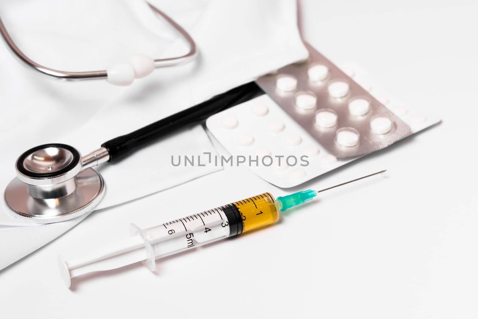 syringe, stethoscope and pills on a doctor's gown white background and copy space