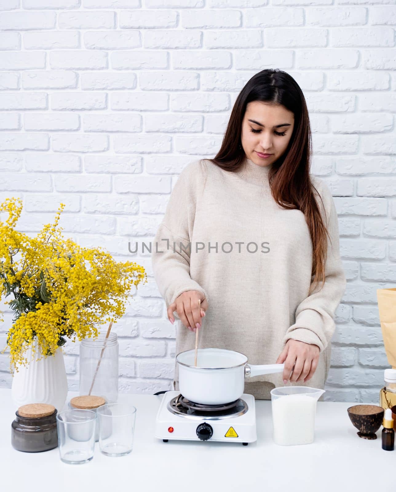 Creative hobby at home. Woman making decorative aroma candle at table, stirring melting soy wax in the pot