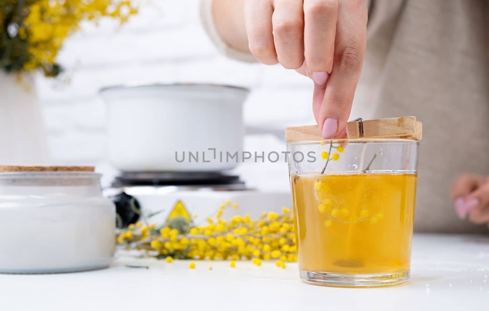 Creative hobby at home. Woman making decorative aroma candle with mimosa flowers at table