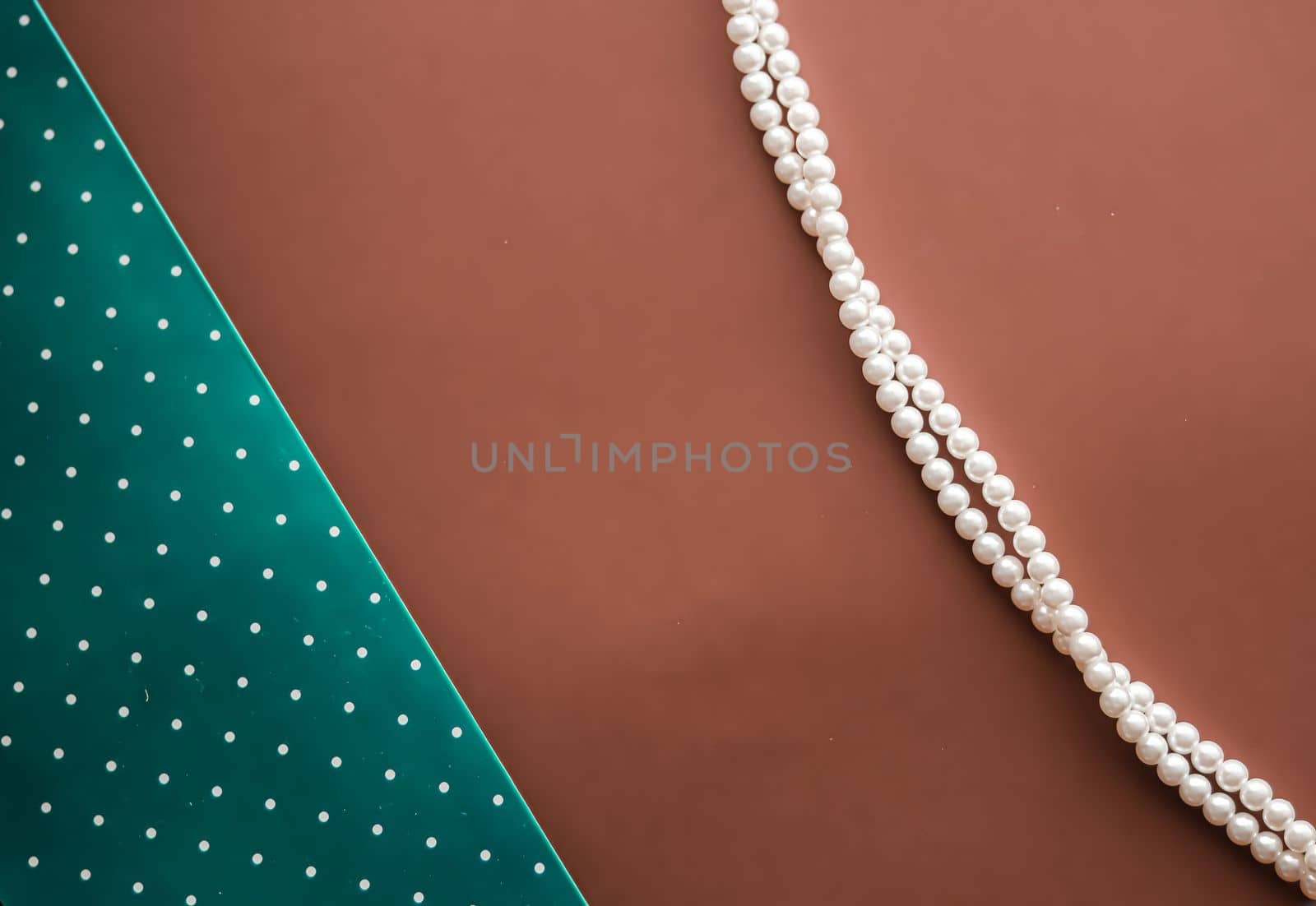 Pearl jewellery necklace and abstract green polka dot background on brown backdrop by Anneleven
