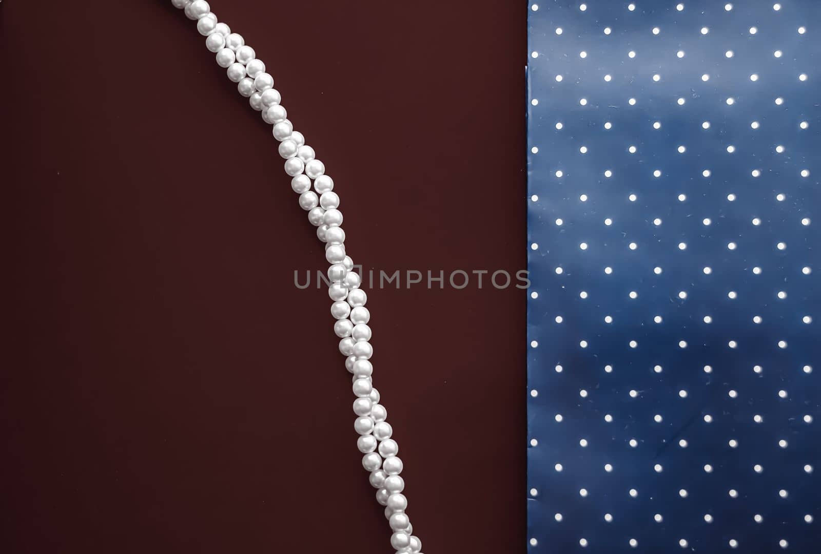 Pearl jewellery necklace and abstract blue polka dot background on chocolate backdrop by Anneleven