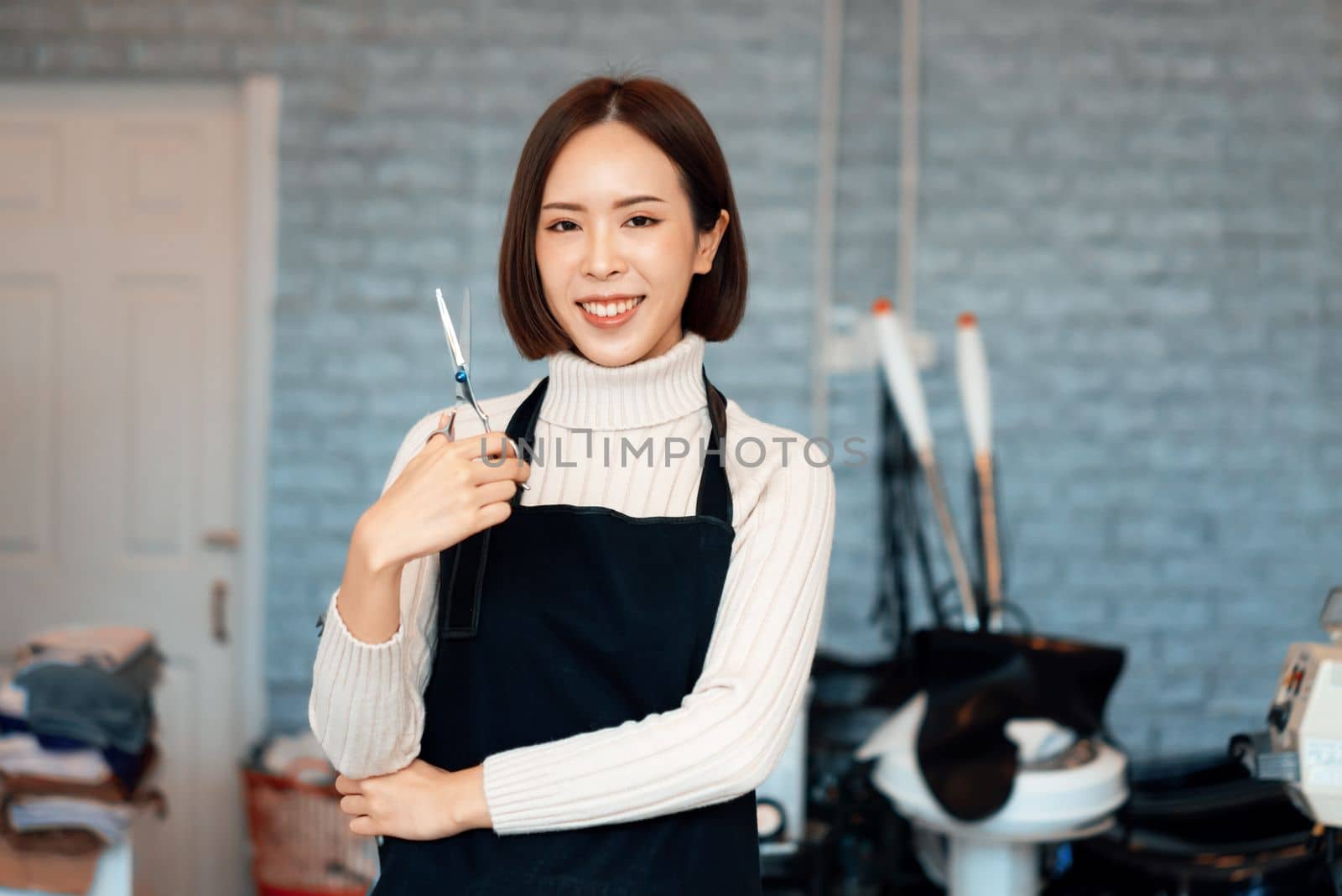 Portrait of a young asian female hairdresser holding qualified haircut tools. by biancoblue