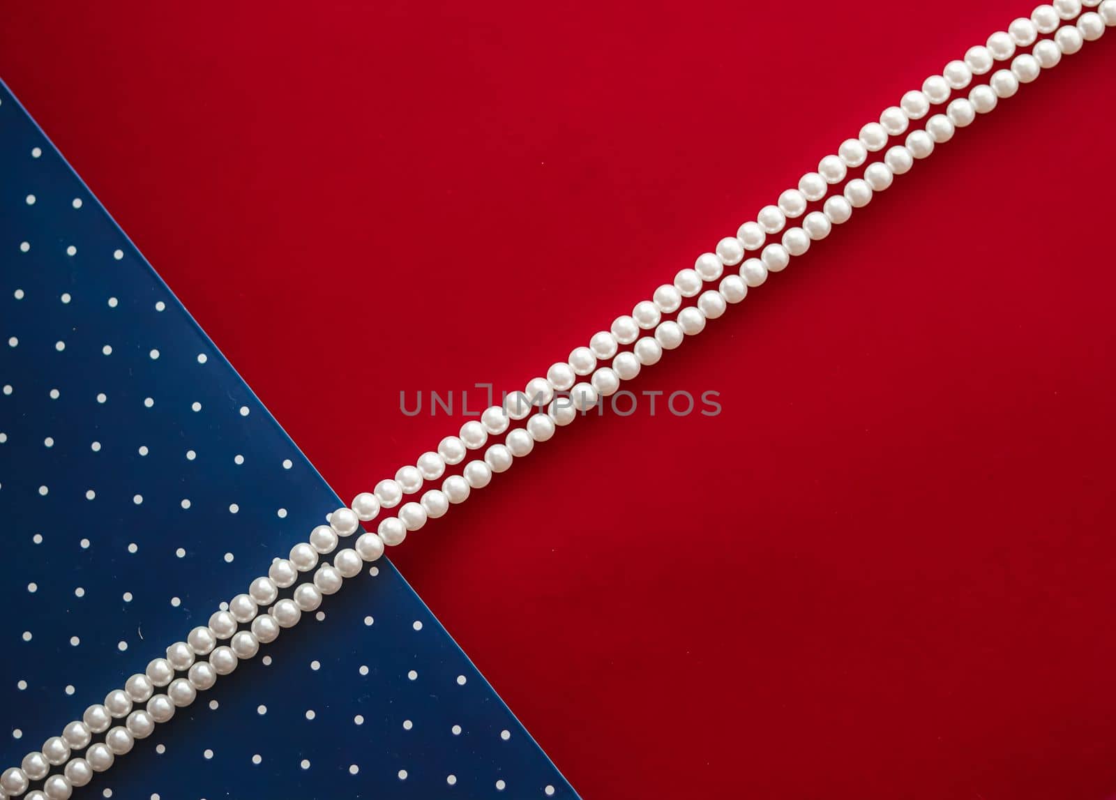 Pearl jewellery necklace and abstract blue polka dot background on red backdrop by Anneleven