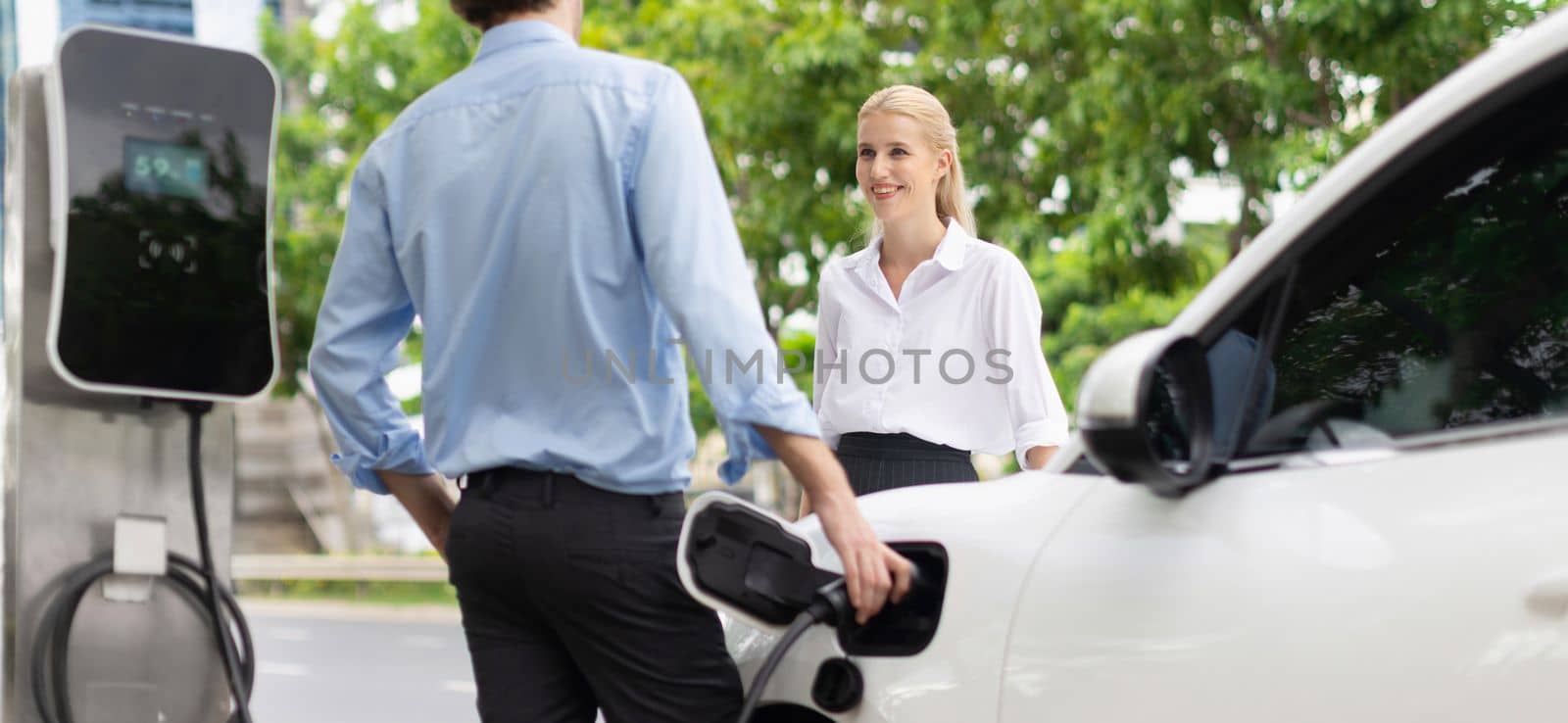Progressive businessman and businesswoman at charging point and EV car by biancoblue