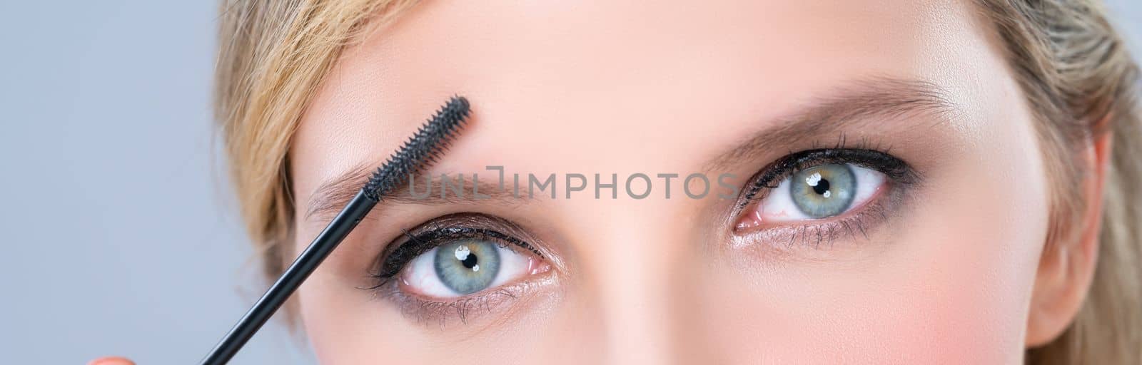 Closeup beautiful woman putting alluring black mascara on long thick eyelashes. by biancoblue