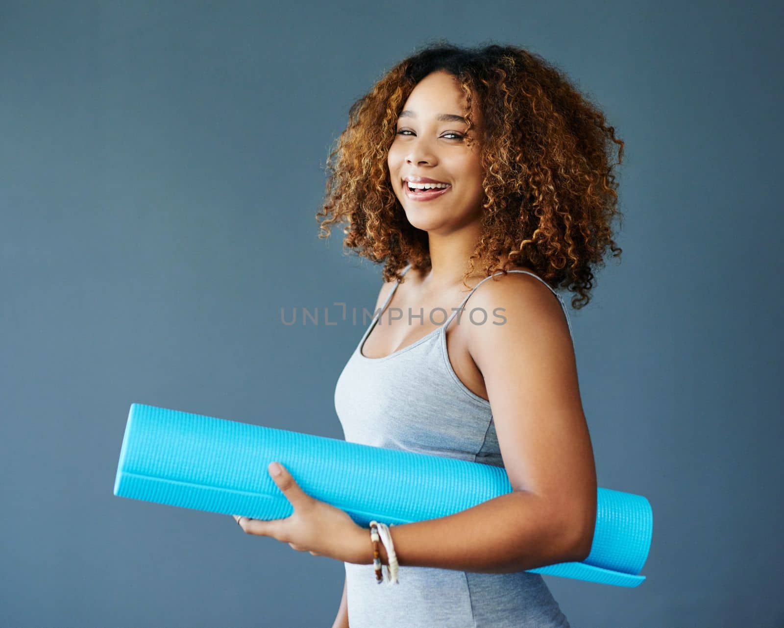 Never underestimate a woman with a yoga mat. a young woman holding a yoga mat against a grey background