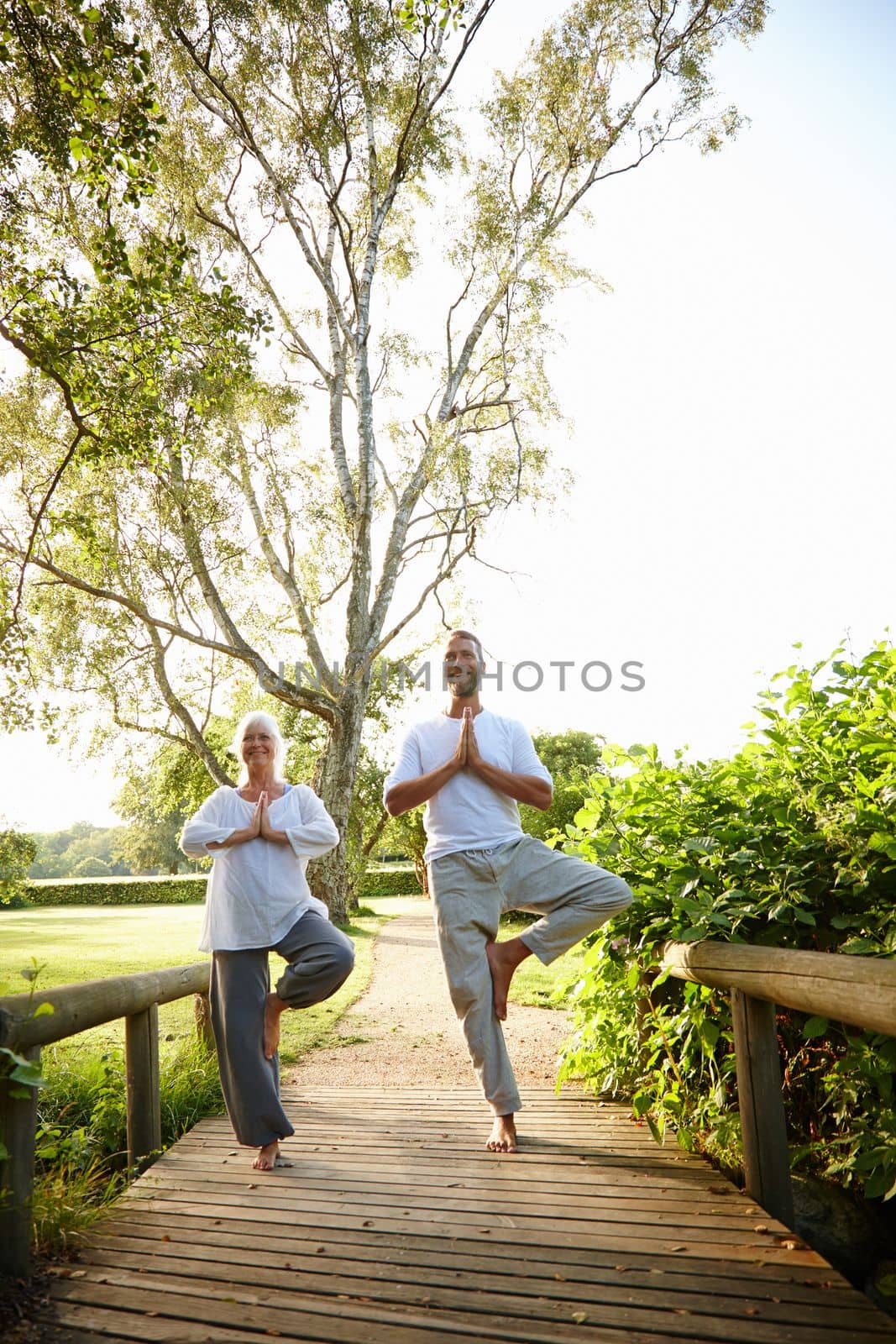 Its all about balance. Full length shot of a mature couple doing yoga together in the outdoors. by YuriArcurs