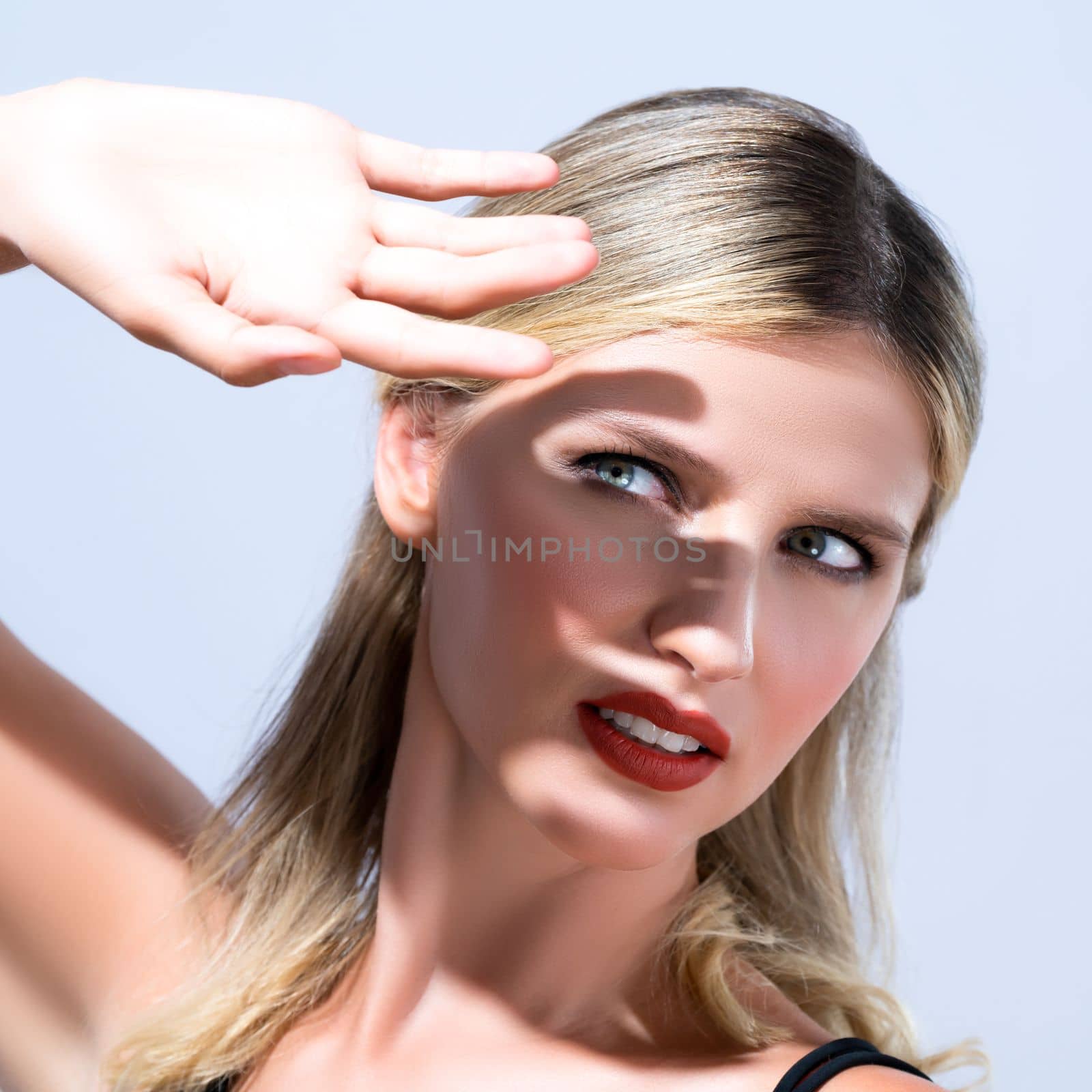 Closeup young blond hair woman with perfect skin and soft alluring facial makeup raise her hand cover her face from bright sunlight in isolated background for skincare sunscreen product.