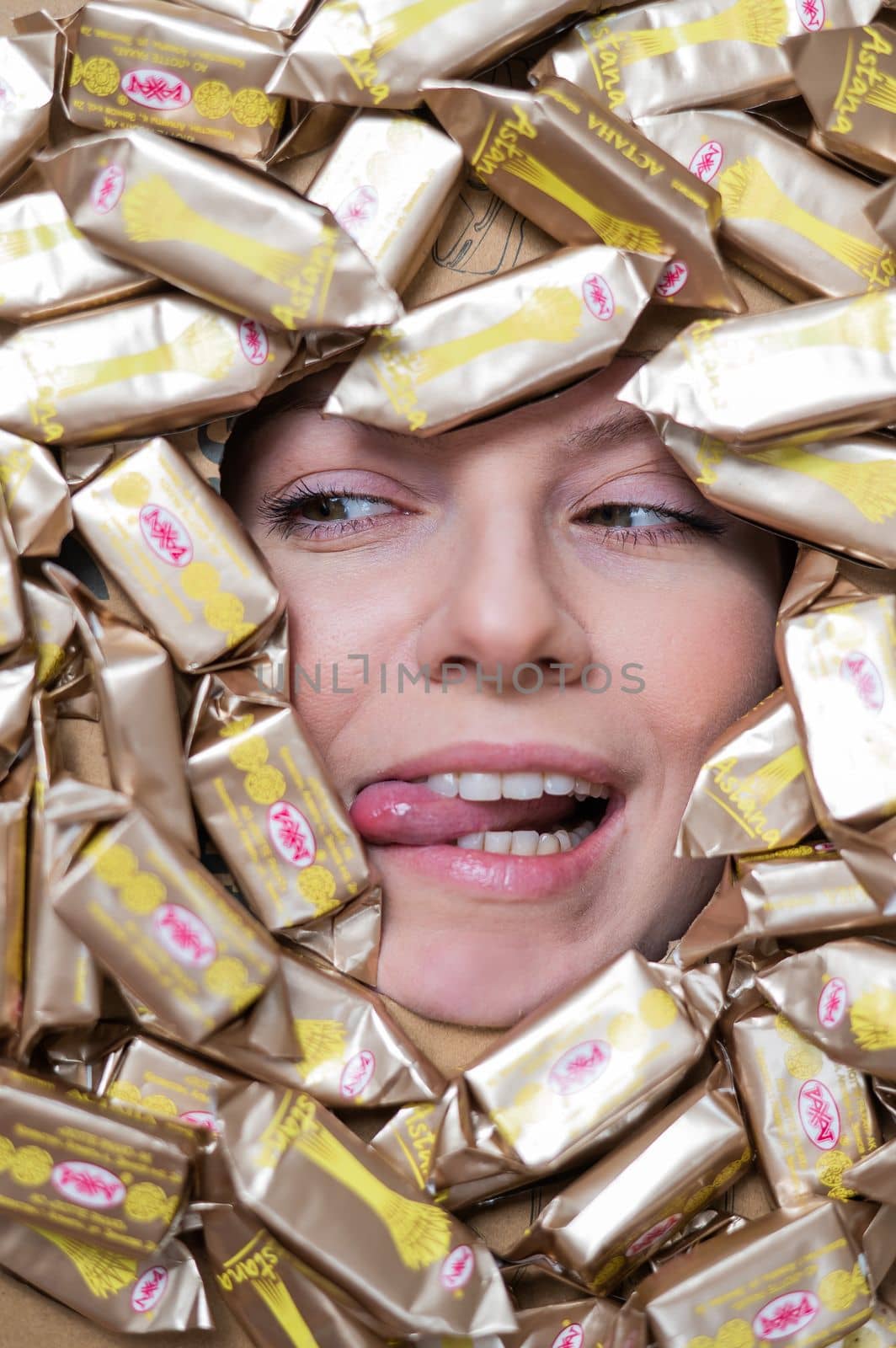 The face of a Caucasian woman surrounded by Rakhat chocolates. The girl shows her tongue. by mrwed54